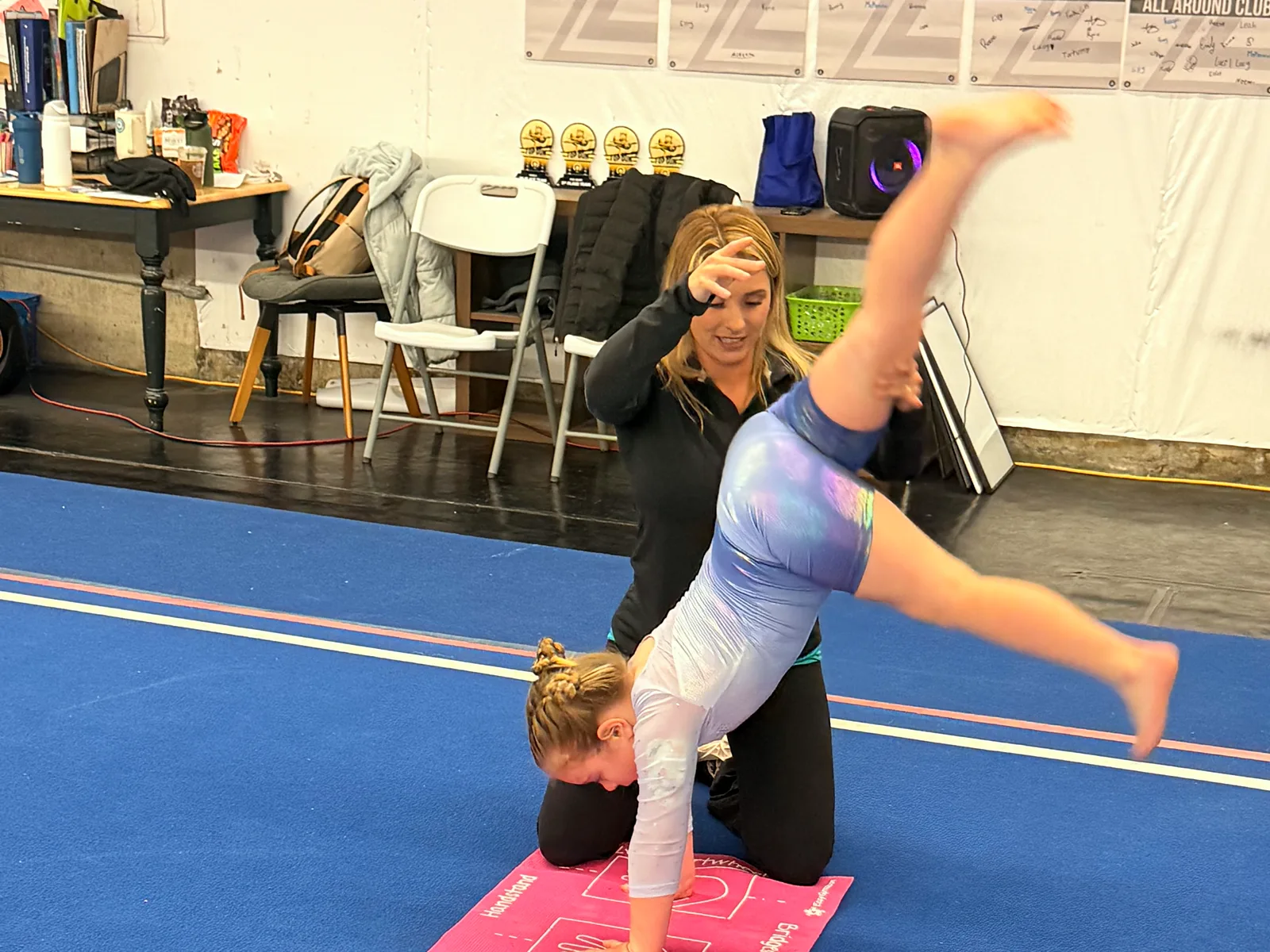 A PEGA coach spotting a gymnast through a cartwheel