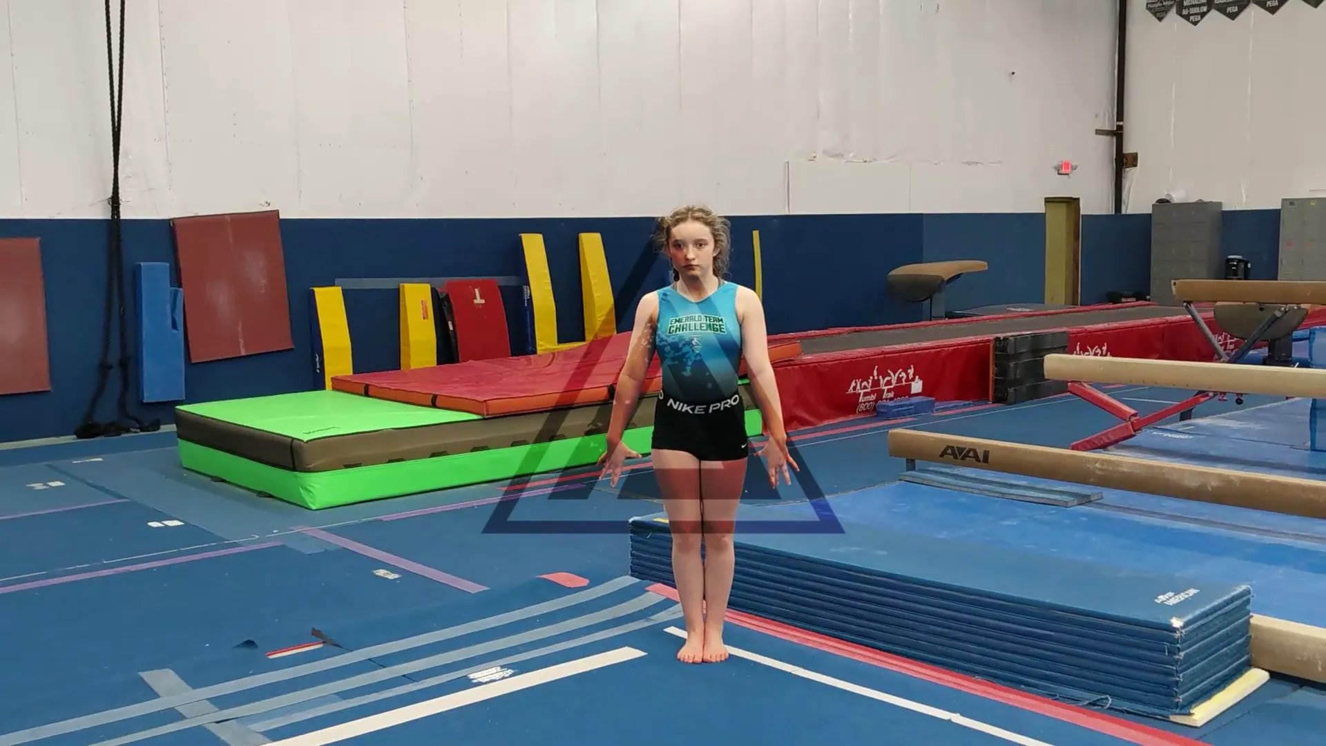 A PEGA gymnast standing on the floor of the gym, beams and mats behind her