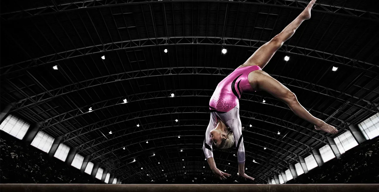 A PEAK Elite gymnast mid-leap on the beam under arena lights